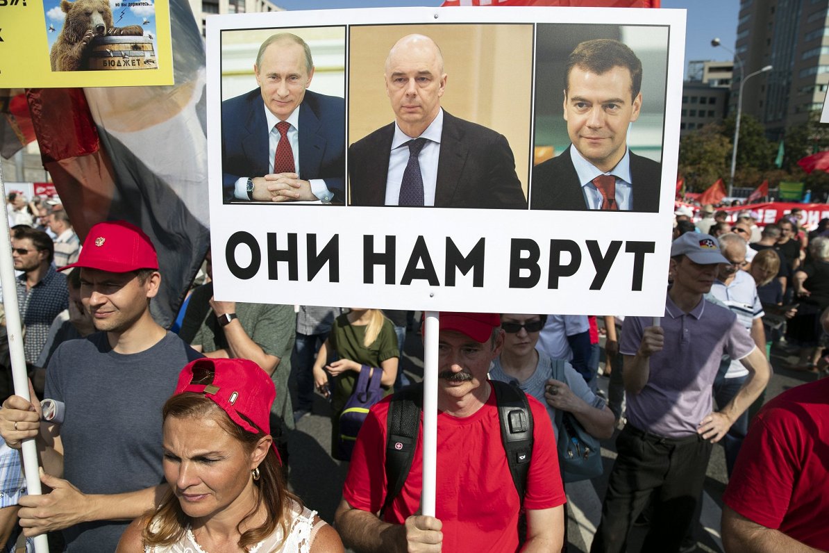 Krievijas kompartijas atbalstītāji ar plakātu, uz kura attēloti Krievijas līderi un sauklis &quot;Vi...