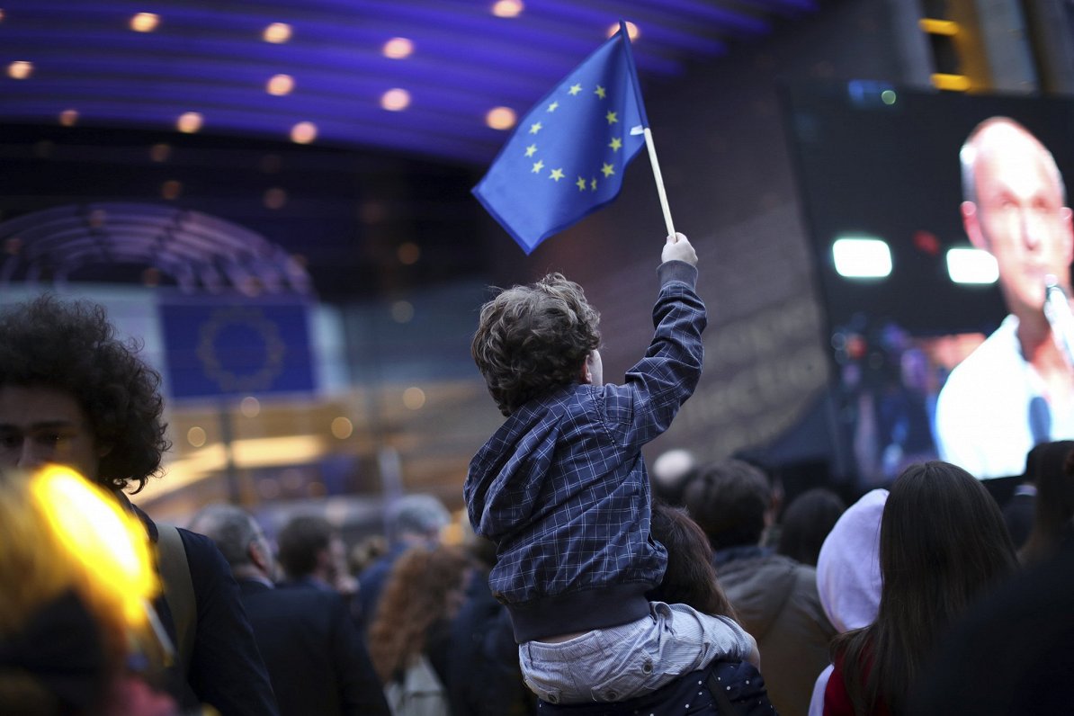 Ilustratīvs attēls: puisēns ar Eiropas Savienības karogu pie Eiropas Parlamenta ēkas Briselē