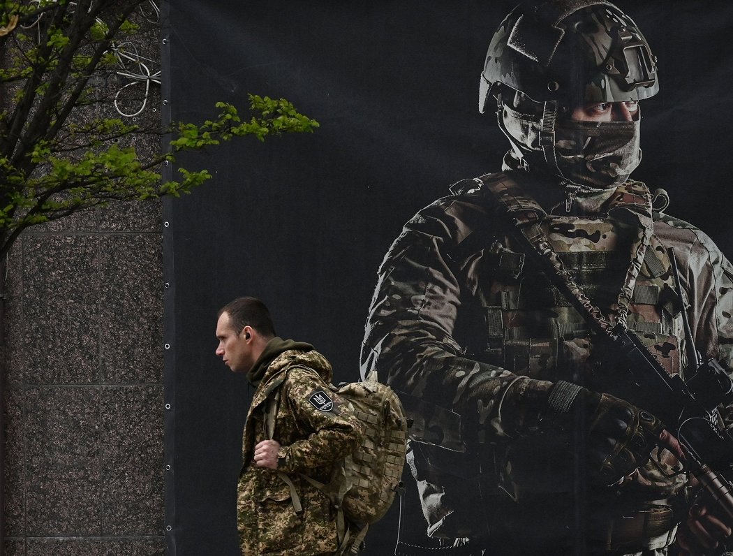 Ukraiņu karavīrs pie plakāta Kijivā.