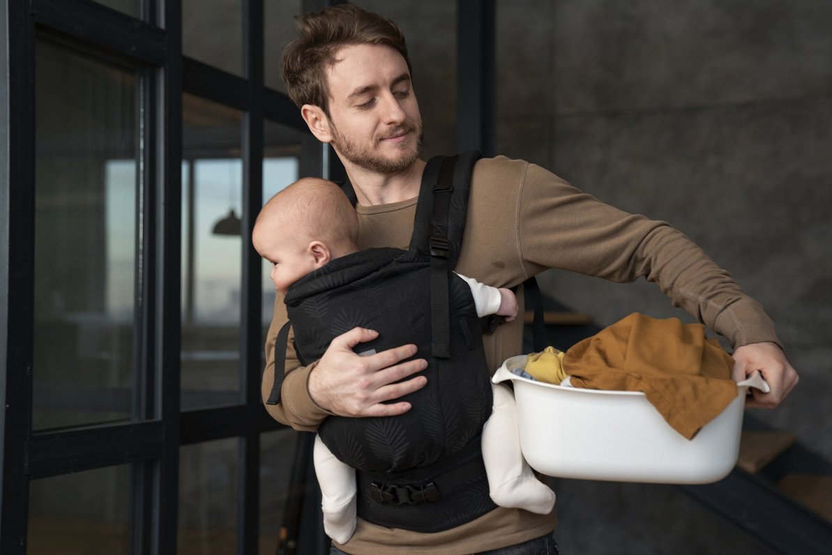 Vīrietis veic mājas darbus un aprūpē mazuli. Attēls ilustratīvs