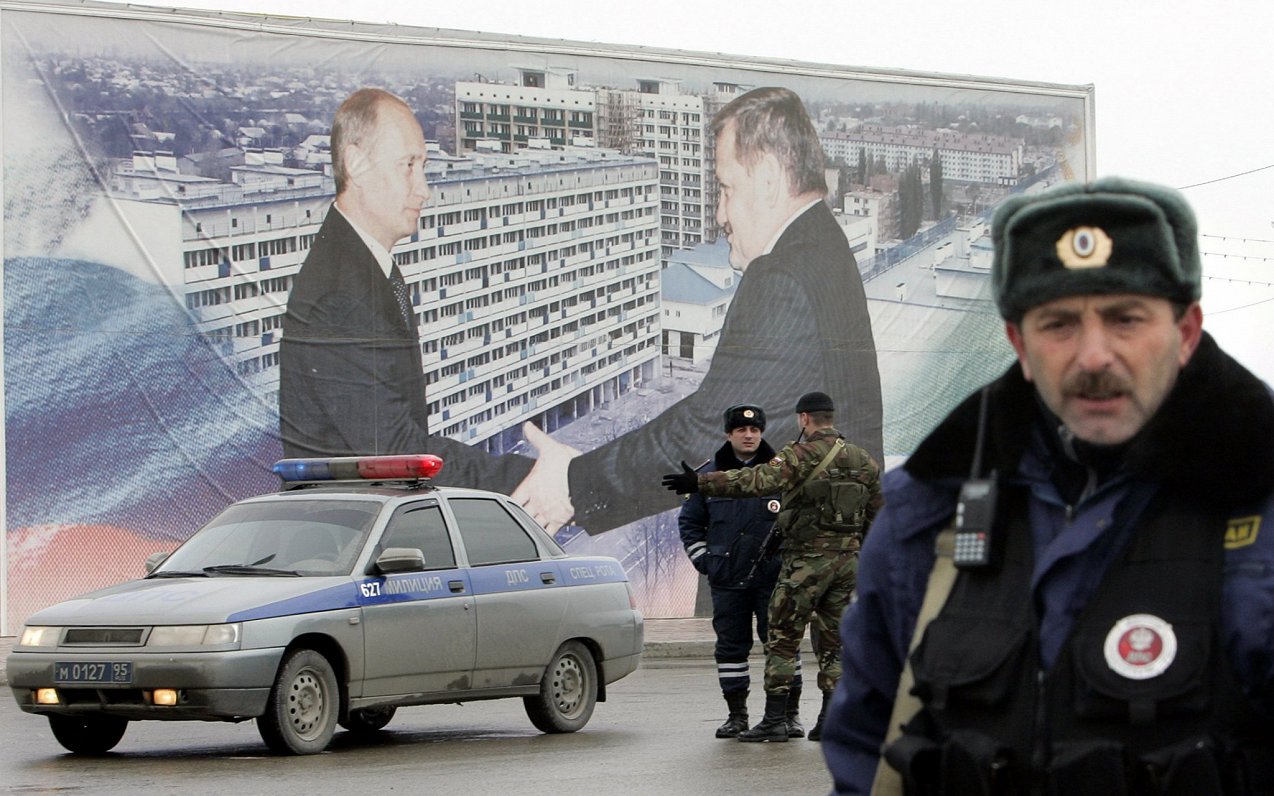 Čečenijas ceļu policijas darbinieki apsargā laukumu pie plakāta Groznijā, uz kura redzams Krievijas...