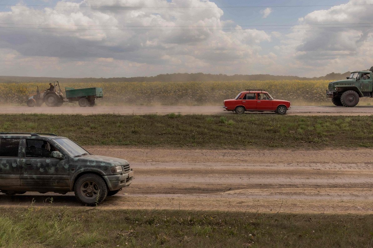 Militārie un civilie transportlīdzekļi brauc gar saulespuķu lauku Sumu reģionā.