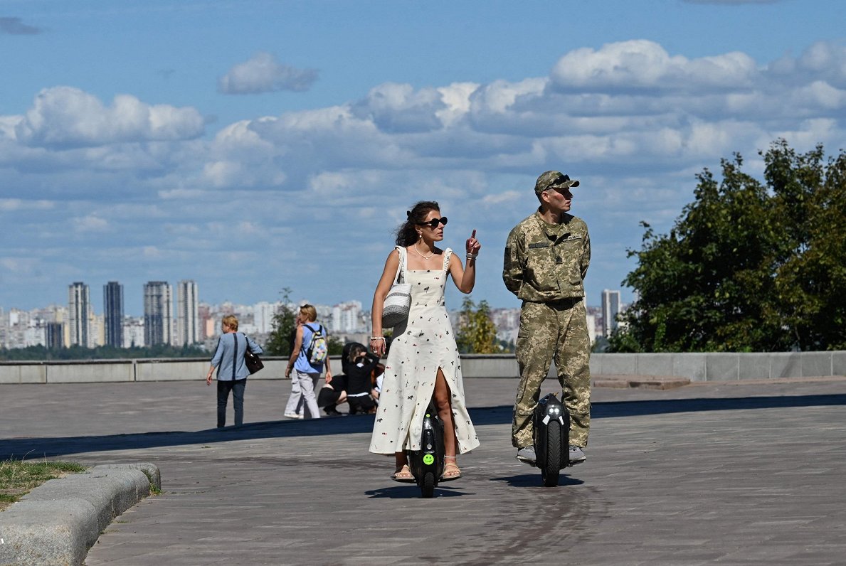 Ukrainas armijas karavīrs un sieviete brauc pa Kijivas parku ar motorizētiem vienriteņiem.