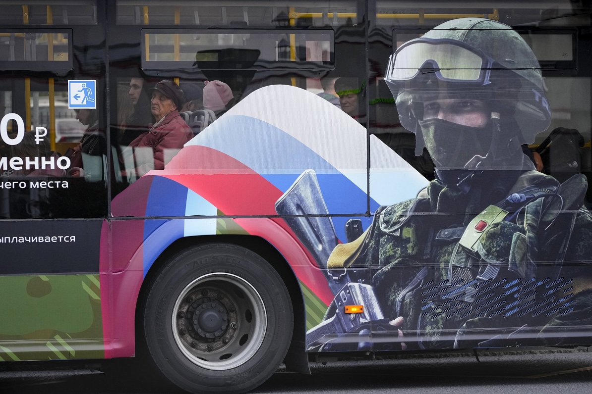 Cilvēki autobusā, uz kura reklamē iesaukšanu Krievijas armijā.