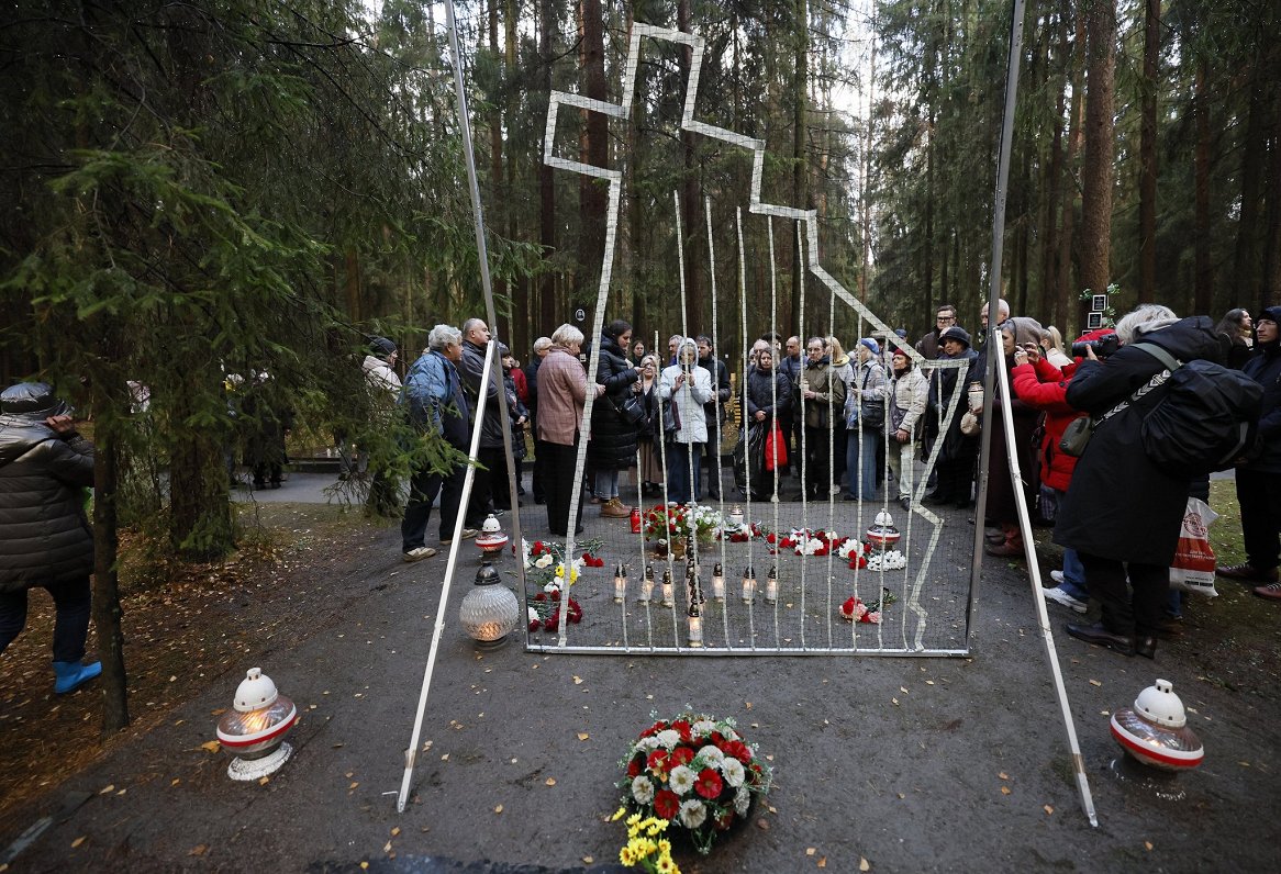 Cilvēki noliek ziedus un svecītes pie politiski represēto poļu apbedījumiem Ļevašovas memoriālajos k...